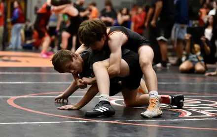 An AWC wrestler in orange and black works a leg ride at a tournament
