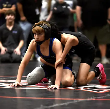 A girl in a blue singlet works from the top position during a tournament match