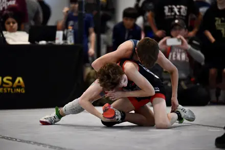 Two boys battle on the mat with a third wrestler working the edge