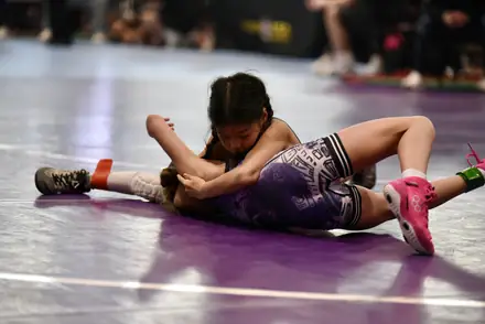 Two young AWC girls locked up on the mat during a match at a state tournament