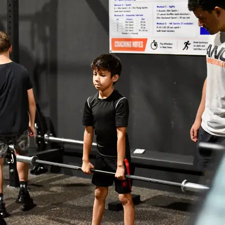A young athlete learning barbell technique with light weight.