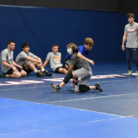 Young wrestlers kneeling on the mat listening to a coach.