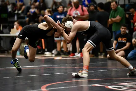 Two wrestlers in black singlets tie up during a tournament bout